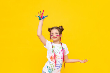 The child is playing with colorful paints. A little girl stained with paint for drawing on a yellow isolated background. Art courses for schoolchildren. Creative education of children.