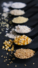 Obraz na płótnie Canvas Colección de cucharas con diferentes cereales y semillas ordenadas en vertical sobre fondo negro. Dark food