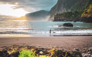 Woman walking on beautiful beach and enjoying the atmospheric morning atmosphere. Seixal beach, Madeira Island, Portugal, Europe. - obrazy, fototapety, plakaty