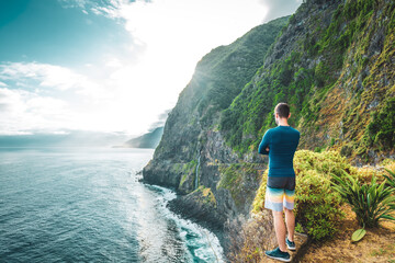 Sporty man looking at waterfall flowing into the sea in atmospheric morning atmosphere. Viewpoint Véu da Noiva, Madeira Island, Portugal, Europe.