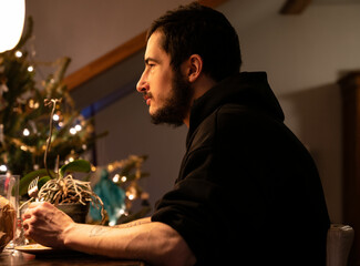 Young man sitting at the table with Christmas tree behind