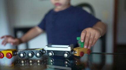 Small boy playing with toys. Child plays alone at home with traditional wooden train toy