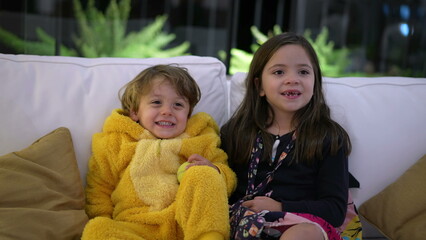 Cute little brother and sister sitting on sofa at living room smiling. Portrait of two siblings smiling posing for camera