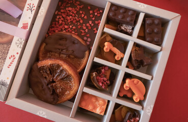 Chocolate candies in a red craft box wooden Christmas background fir branches of a New Year's toy. Flat layout top view.  Chocolate mediants, bites, candies in a gift box for Christmas and New Year ce