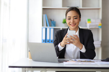 Attractive Asian businesswoman in office checking work schedule on smartphone.