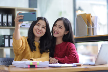 Happy female colleagues using mobile phones to take selfies together.