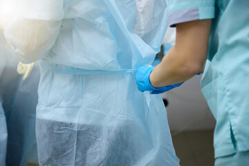 Nurse ties a sterile gown to the surgeon before the operation. Doctors prepare for surgery in the operating room, put on a medical uniform