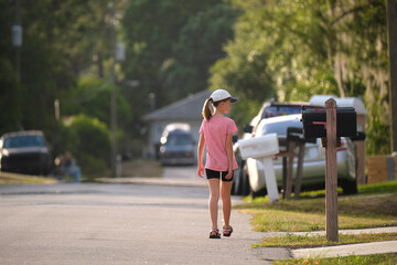 Rear view of confident young child girl walking along the sunny alley. Active lifestyle on summer holidays