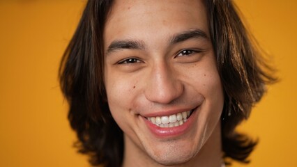 Closeup portrait of young gender fluid man 20s winking at camera isolated on solid yellow background.