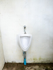 The dirty urinal of the open air toilet near the white wall.