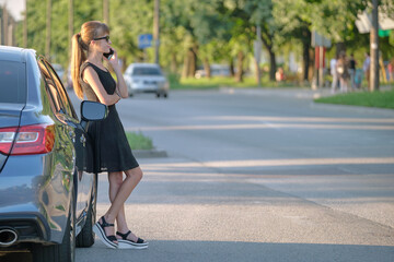 Young female driver standing near her car talking on mobile phone on a city street in summer