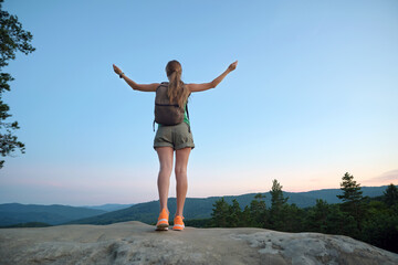 Obraz premium Young woman hiker standing alone with outstretched arms on mountain footpath enjoying view of evening nature on wilderness trail. Active way of life concept
