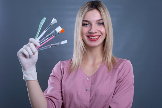 a young girl doctor holds cosmetic brushes for skin procedures in her hands. On a gray background