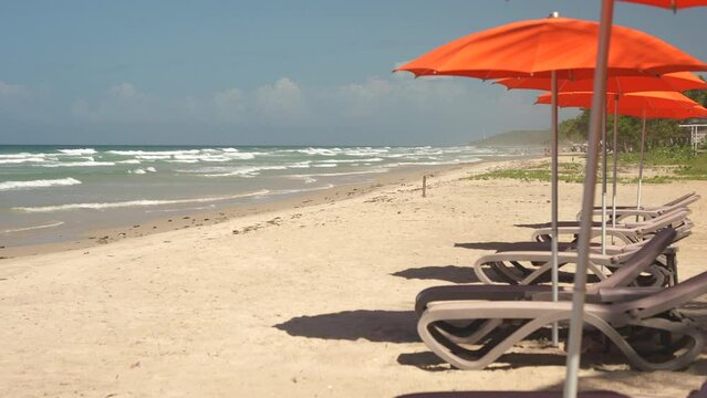 Slow motion sea view through the empty orange parasols and sun loungers on the foreground. Vacation in the all inclusive hotel on the tropical beach 