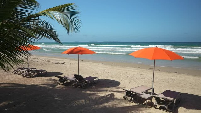 Three empty sun loungers on the tropical beach at sunset. Orange parasols and a beautiful view of the ocean. Vacation in the all inclusive hotel 