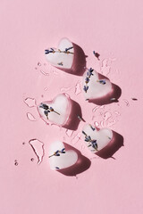 Heart shaped ice cubes with natural lavender flowers on a pink background. Flat lay, vertical image.