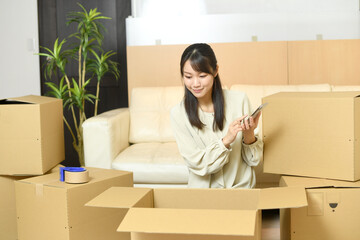 段ボールの前でスマホを持つ若い女性