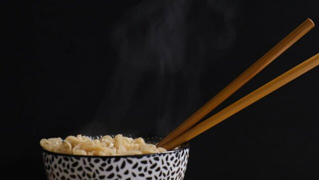 4k v&iacute;deo. Slow motion humo saliendo de unos fideos chinos colocados en un cuenco blanco y negro con palillos chinos, sobre un fondo negro hasta desaparecer. Dark food
