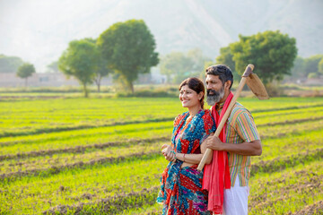 Indian farmer holding spade in hand and standing with wife at agriculture field.