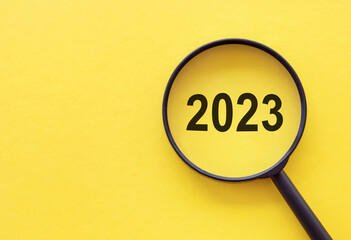Magnifying glass magnifies the year 2023 on yellow background. Focusing on the year 2023 for...