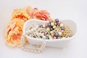 Multi-colored jewelry and costume jewelry in a white bathroom surrounded by yellow-pink flowers. Copy space