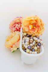 Multi-colored jewelry and costume jewelry in white bathroom surrounded by yellow-pink flowers. Close up