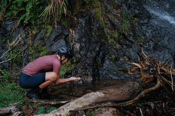 A young female cyclist is washing her hands by the creek