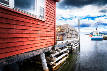 Fototapeta na wymiar Boat shed and dock loaded with lobster traps overlooking a small harbour with fishing boats near Trinity Newfoundland.