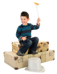 An isolated boy in jeans and a striped pullover sitting on some old suitcases plays with a wand.