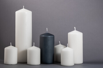 Six different white candles and one black on a dark gray background.