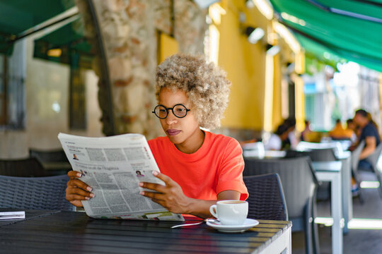 Woman drinking coffee and reading newspaper at cafe. Leisure and news concept