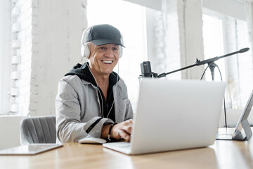 The man works on the radio, online communication broadcast. Workplace in the studio, uses laptop equipment, headphones, microphone.