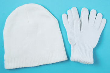 White knitted winter hat and gloves on a blue background. View from above.
