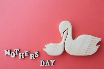 Swans mother and child, light wooden figurines. The inscription next to it is Mother's Day. Concept greeting card. Background red.
