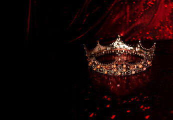 Royal crown with precious gems on red luxury fabric background
