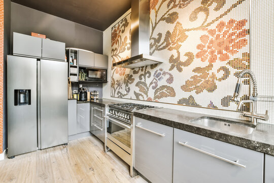 A Modern Kitchen With White Cabinets And Stainless Steel Appliances On The Counter Top Is Decorated With Colorful Tiles In An Artistic Pattern