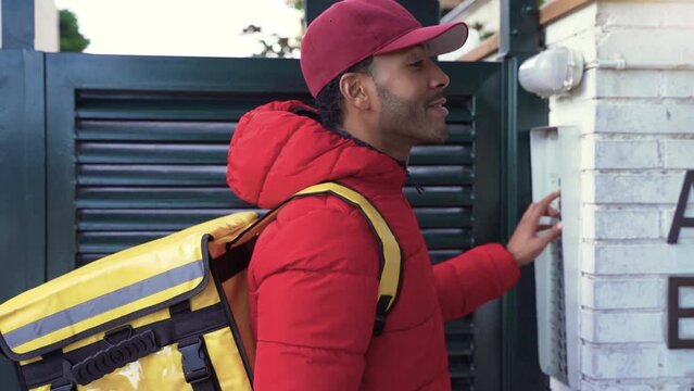 Food delivery concept. Young driver with backpack delivering products at door for customers who order online purchases. Black male happy with his job. High quality 4k footage