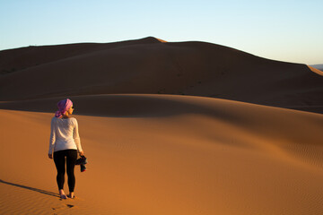 Fototapeta na wymiar backlight of a girl walking barefoot through the sahara desert at sunset