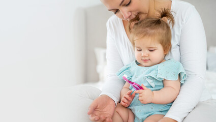 Fototapeta na wymiar Mother brushing baby's first tooth with toothbrush. Happy healthy lifestyle and baby care. Babyhood and parenthood. Copy space for advertisement