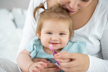 First knowledge of baby with toothbrush. Mom showing to child girl how to brush teeth. Habit of...