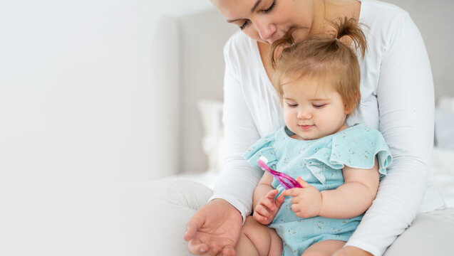 Mother brushing baby's first tooth with toothbrush. Happy healthy lifestyle and baby care. Babyhood and parenthood. Copy space for advertisement