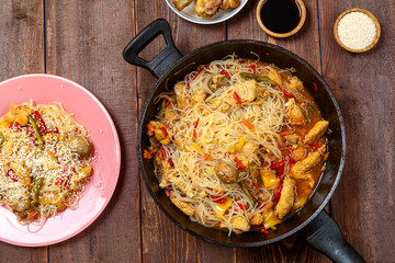 Funchoza with chicken and vegetables in teriyaki and oyster sauce in a frying pan on a wooden table...