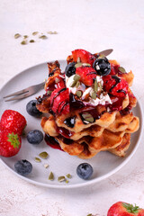 Stack of waffles with strawberry, blueberry, whipped cream and chocolate sauce on ceramic plate on white table. Appetizing dessert
