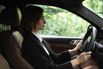 Fototapeta na wymiar Portrait of young attractive business woman in black suit driving in her luxury car. Business transportation concept