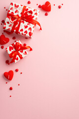 Saint Valentine's Day concept. Top view vertical photo of gift boxes with ribbon bows heart shaped candles and sprinkles on isolated pastel pink background with copyspace