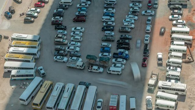 Aerial view of a parking lot with many cars and buses in rows timelapse during all day with shadows moving fast. Free area on a sand