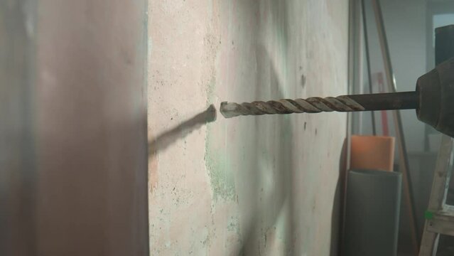 Process of drilling hole in concrete wall using electric drill or perforator. Close up of metal chuck with an auger drill rotating. In process of drilling with drill, white dust from plaster crumbles.