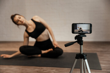 fitness woman make stretching exercises in front camera on tripod at home.
