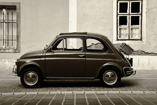 vintage stylish retro Fiat 500 cc car. grunge stucco facade of old house in the background. artistic side perspective view. wicker picnic basket attached. soft sepia finish. 