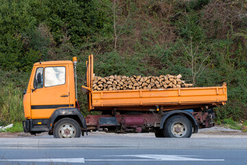 An orange-colored truck loaded with a large amount of firewood for heating the premises. Firewood for the stove during the winter cold. The war in Ukraine. Freezing vropa